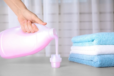 Photo of Woman pouring laundry detergent into cap on table against blurred background, closeup