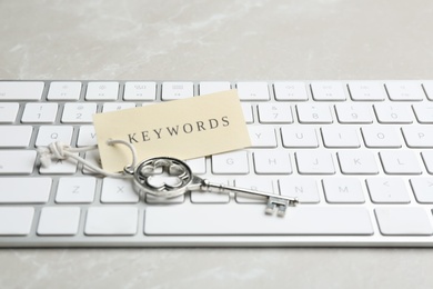 Photo of Keyboard, vintage key and tag with word KEYWORDS on light grey table, closeup