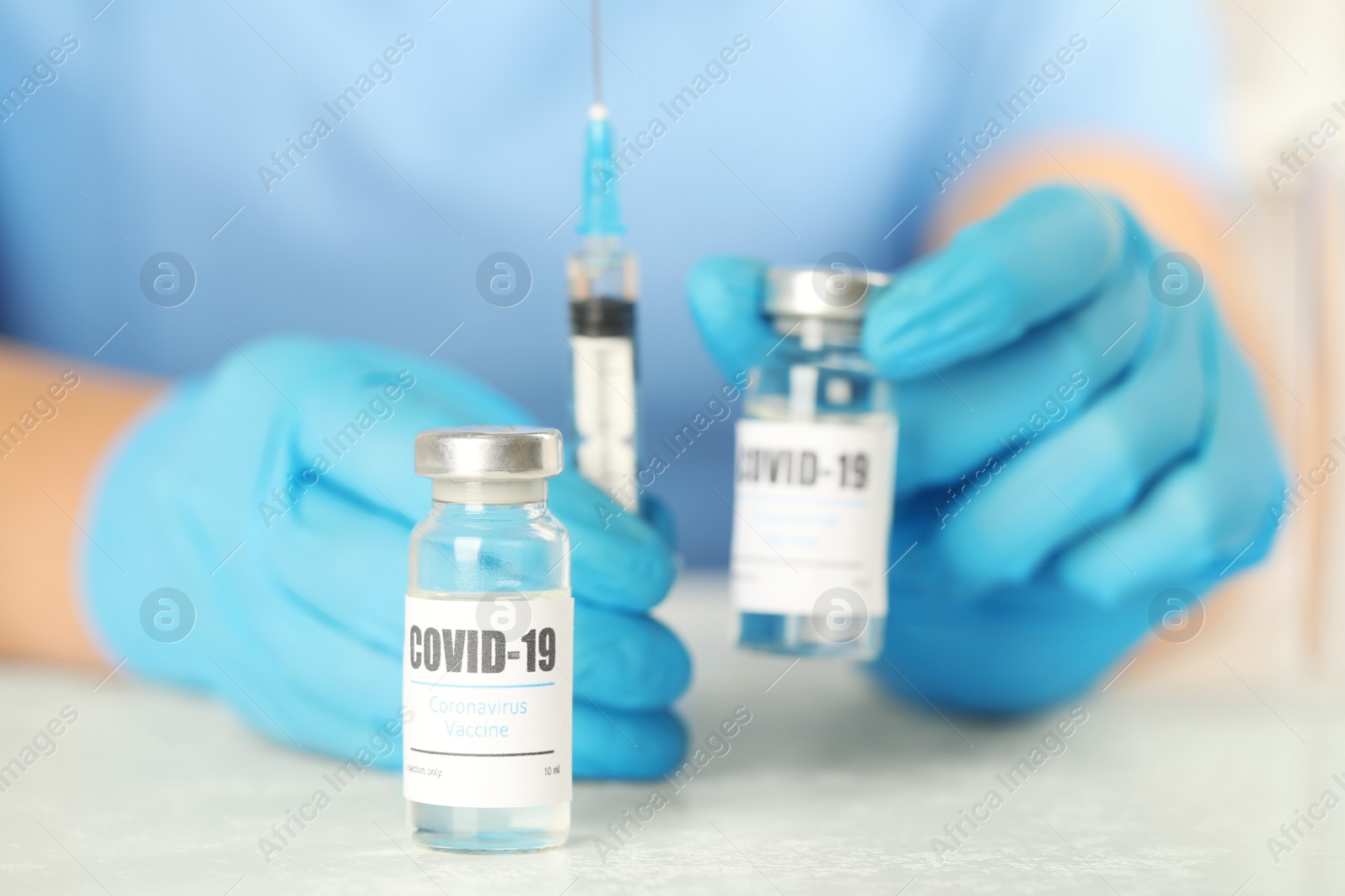 Photo of Doctor with coronavirus vaccine and syringe at table in laboratory, closeup