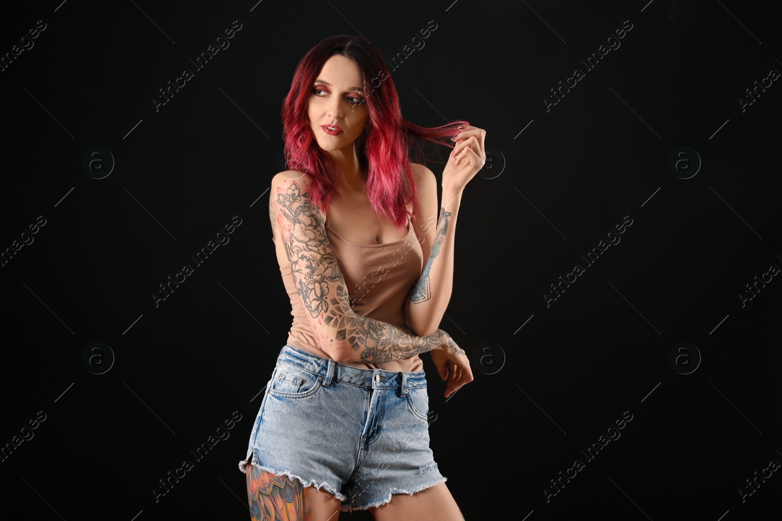 Photo of Beautiful woman with tattoos on body against black background