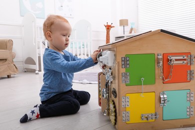 Photo of Cute little boy playing with busy board house on floor at home