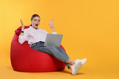 Photo of Emotional woman with laptop sitting on beanbag chair against on orange background. Space for text