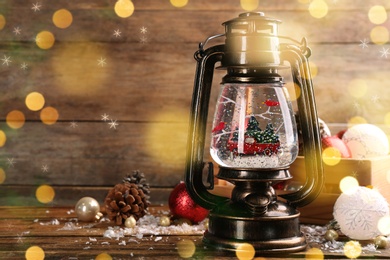 Beautiful Christmas snow globe in vintage lantern and festive decor on wooden table, space for text. Bokeh effect