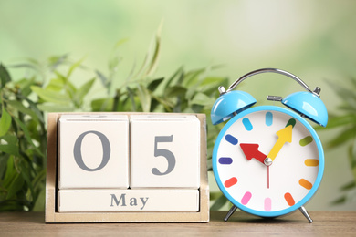 Wooden block calendar and alarm clock on table against blurred green background