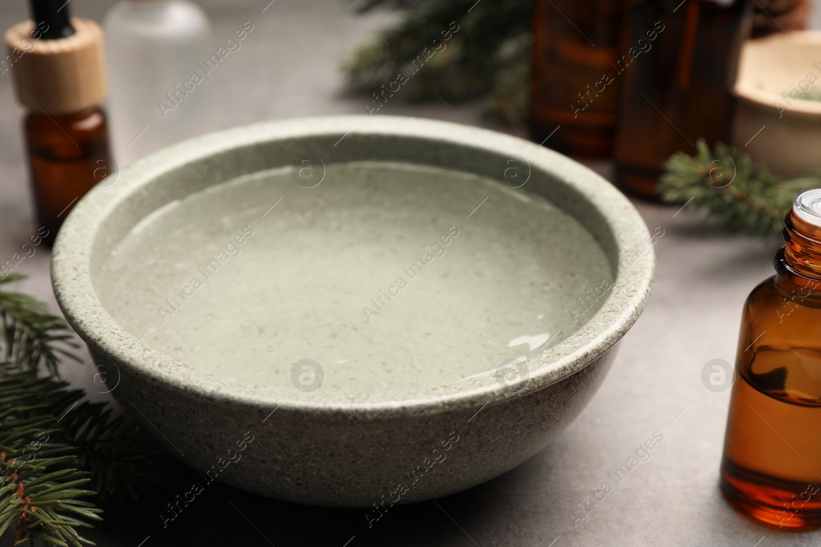 Photo of Bowl of essential oil and fir twigs on grey table, closeup. Aromatherapy treatment