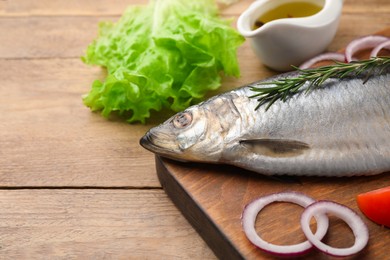 Photo of Board with delicious salted herring and ingredients on wooden table, closeup. Space for text
