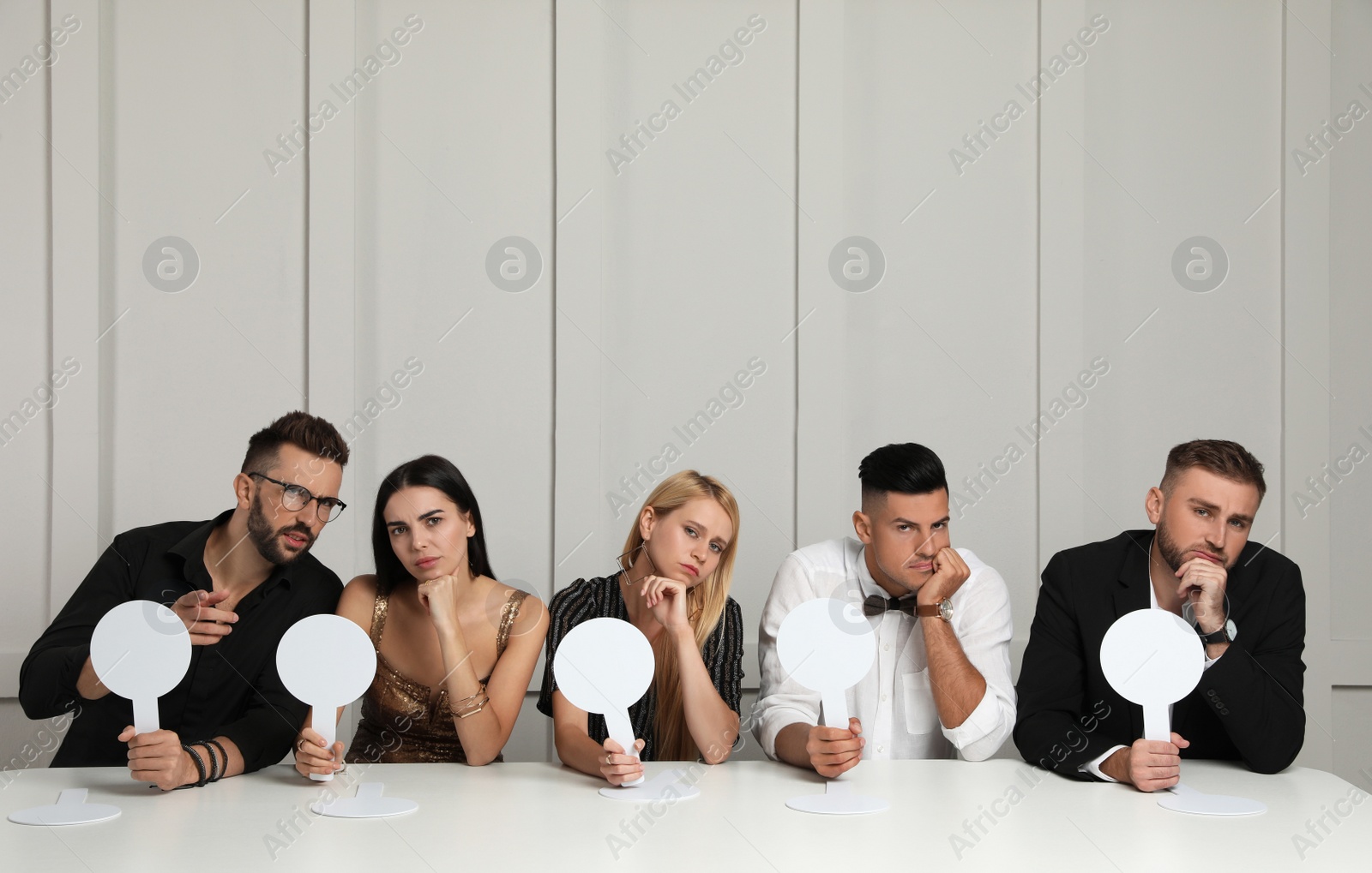 Photo of Panel of disappointed judges holding blank score signs at table against light wall. Space for text