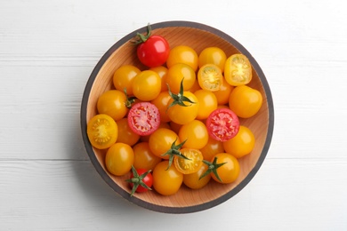 Photo of Ripe red and yellow tomatoes in bowl on white wooden table, top view