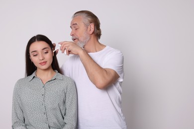 Senior man spraying medication into woman's ear on white background, space for text