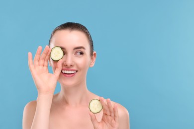 Photo of Beautiful woman covering eye with piece of cucumber on light blue background, space for text