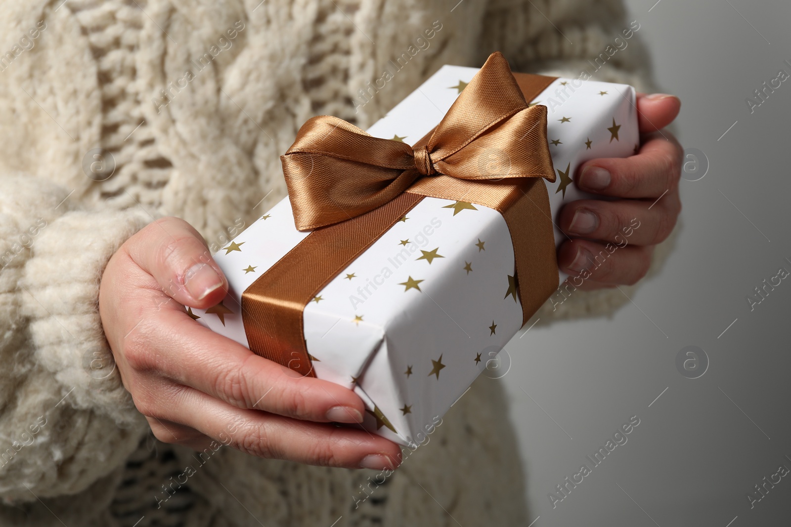 Photo of Christmas present. Woman holding gift box against grey background, closeup