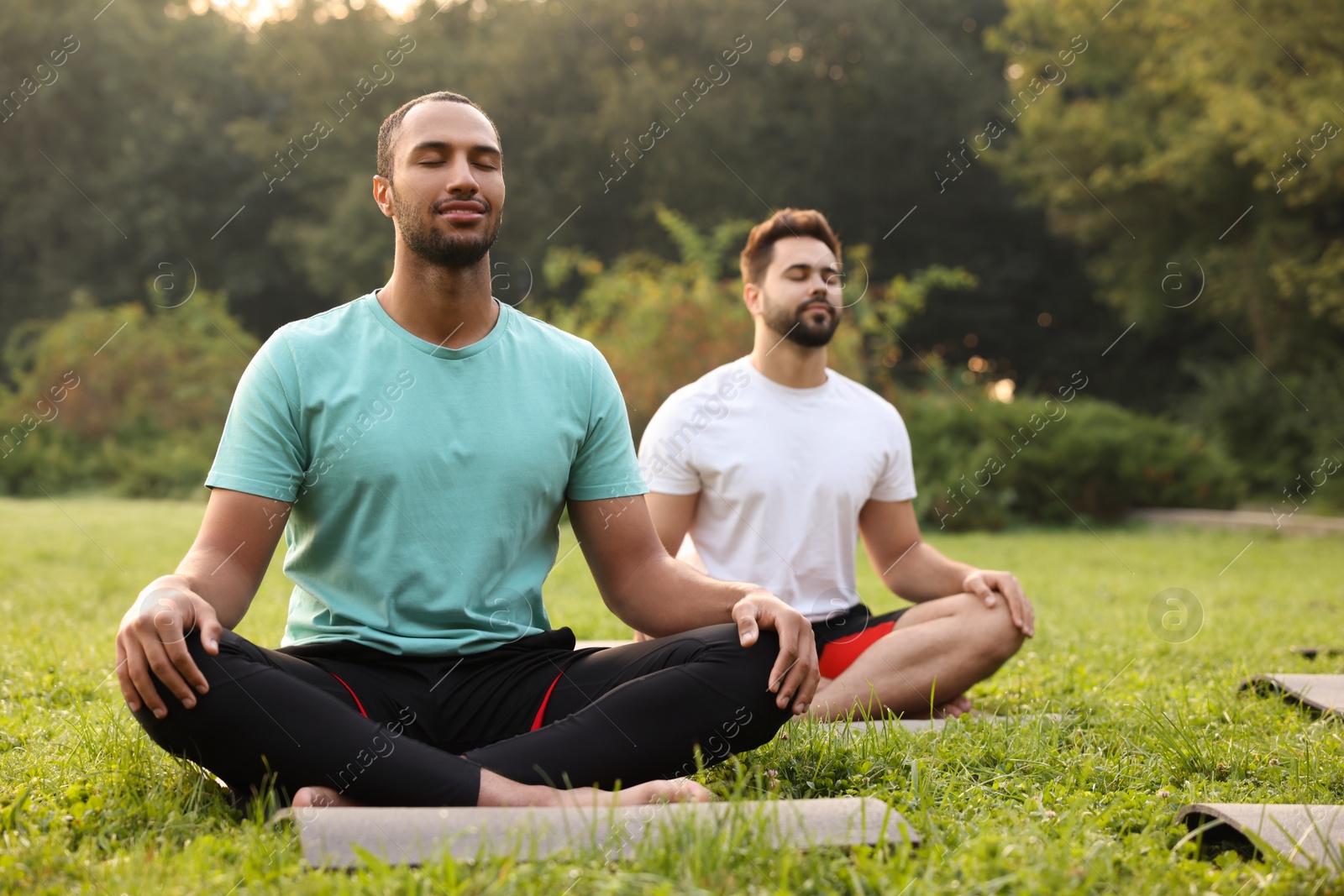 Photo of Men practicing yoga on mats outdoors. Lotus pose