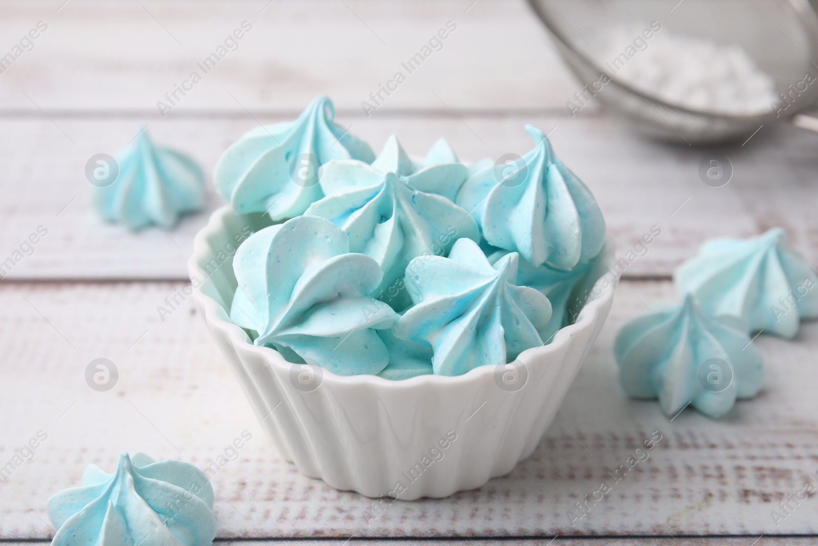 Photo of Tasty meringue cookies in bowl on white wooden table