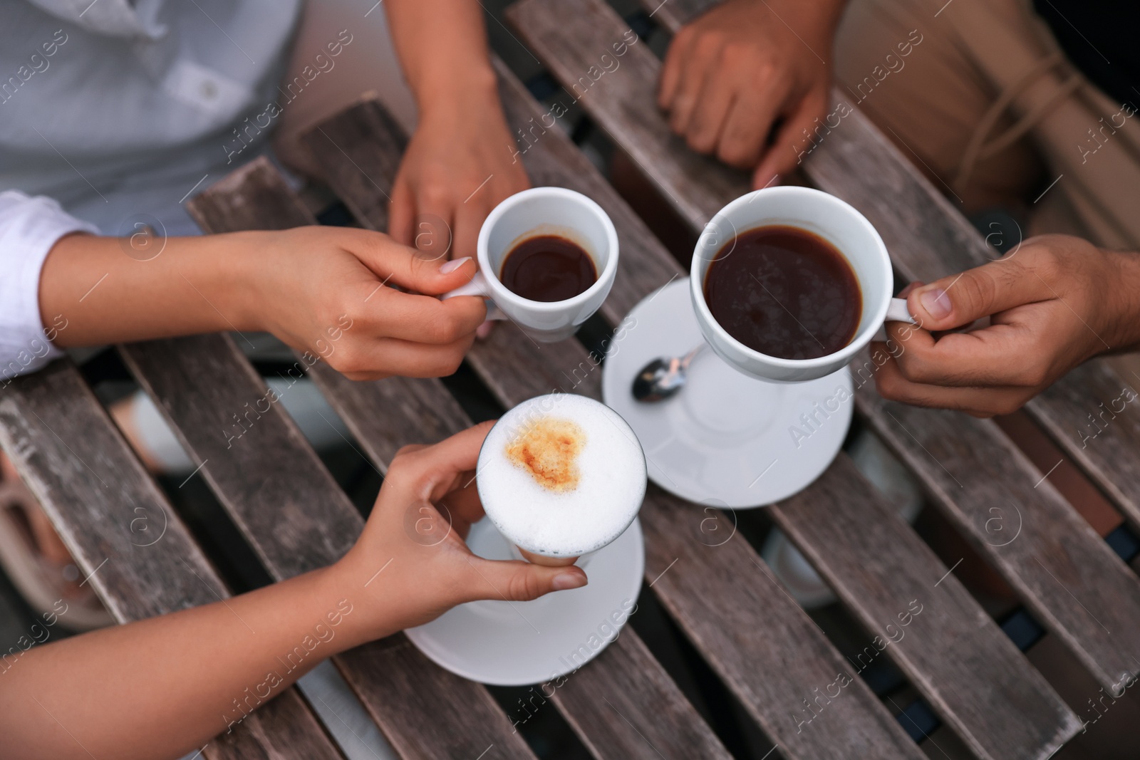 Photo of Friends drinking coffee at wooden table in outdoor cafe, above view