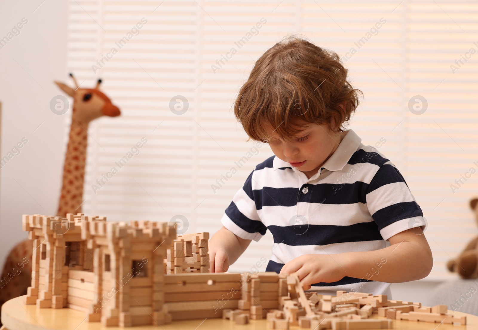 Photo of Cute little boy playing with wooden construction set at table in room. Child's toy