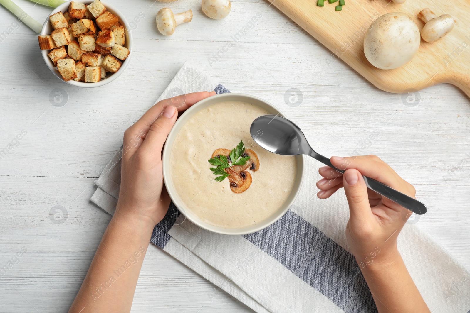 Photo of Woman eating fresh homemade mushroom soup from bowl on table, top view