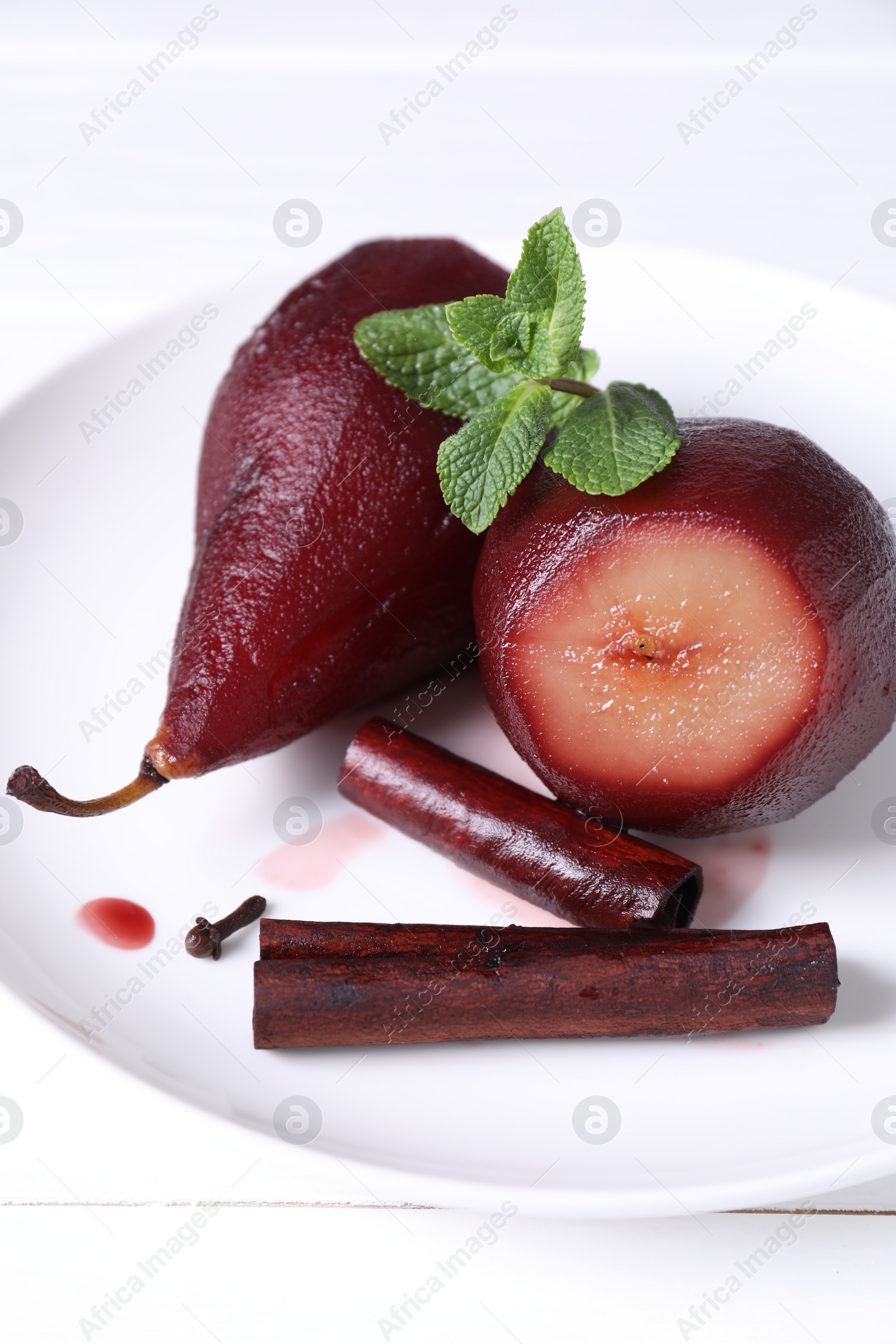 Photo of Tasty red wine poached pears with mint and cinnamon on white wooden table, closeup