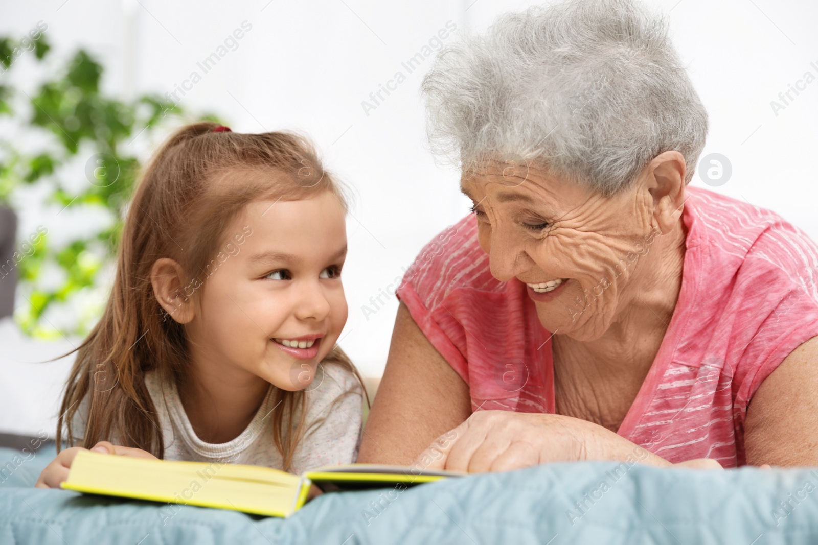 Photo of Cute girl and her grandmother reading book on bed at home