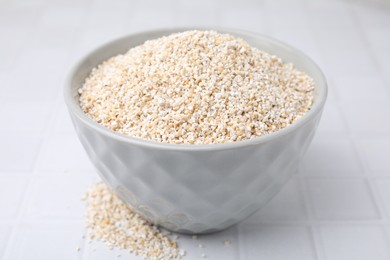 Photo of Dry barley groats in bowl on white tiled table, closeup