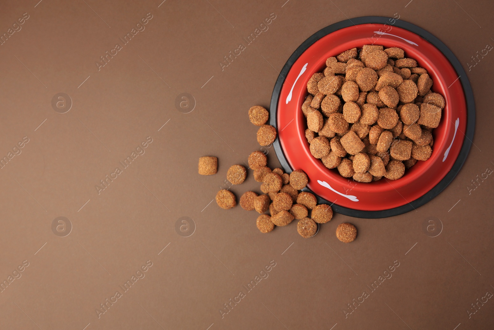 Photo of Dry dog food and feeding bowl on brown background, flat lay. Space for text