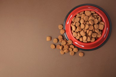 Photo of Dry dog food and feeding bowl on brown background, flat lay. Space for text