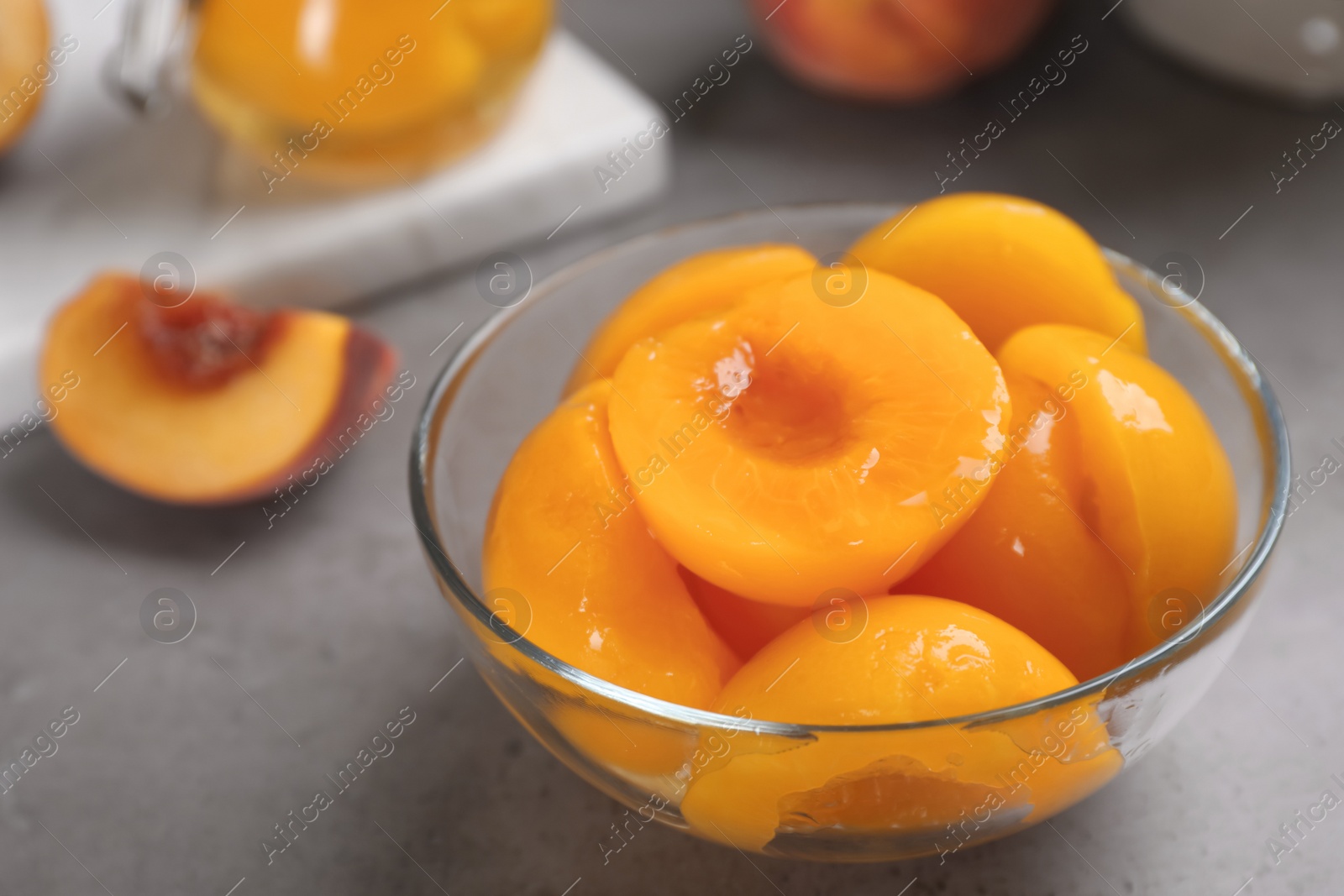 Photo of Glass bowl with conserved peach halves on grey table