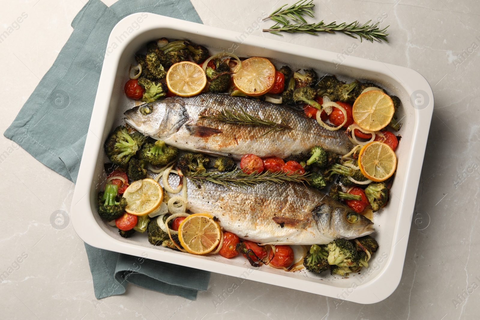 Photo of Delicious fish with vegetables and lemon in baking dish on light marble table, top view