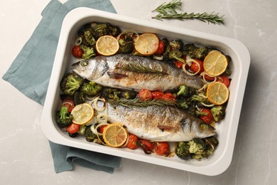 Photo of Delicious fish with vegetables and lemon in baking dish on light marble table, top view