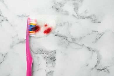 Photo of Brush, toothpaste foam with blood on white marble table, top view and space for text. Gum problems