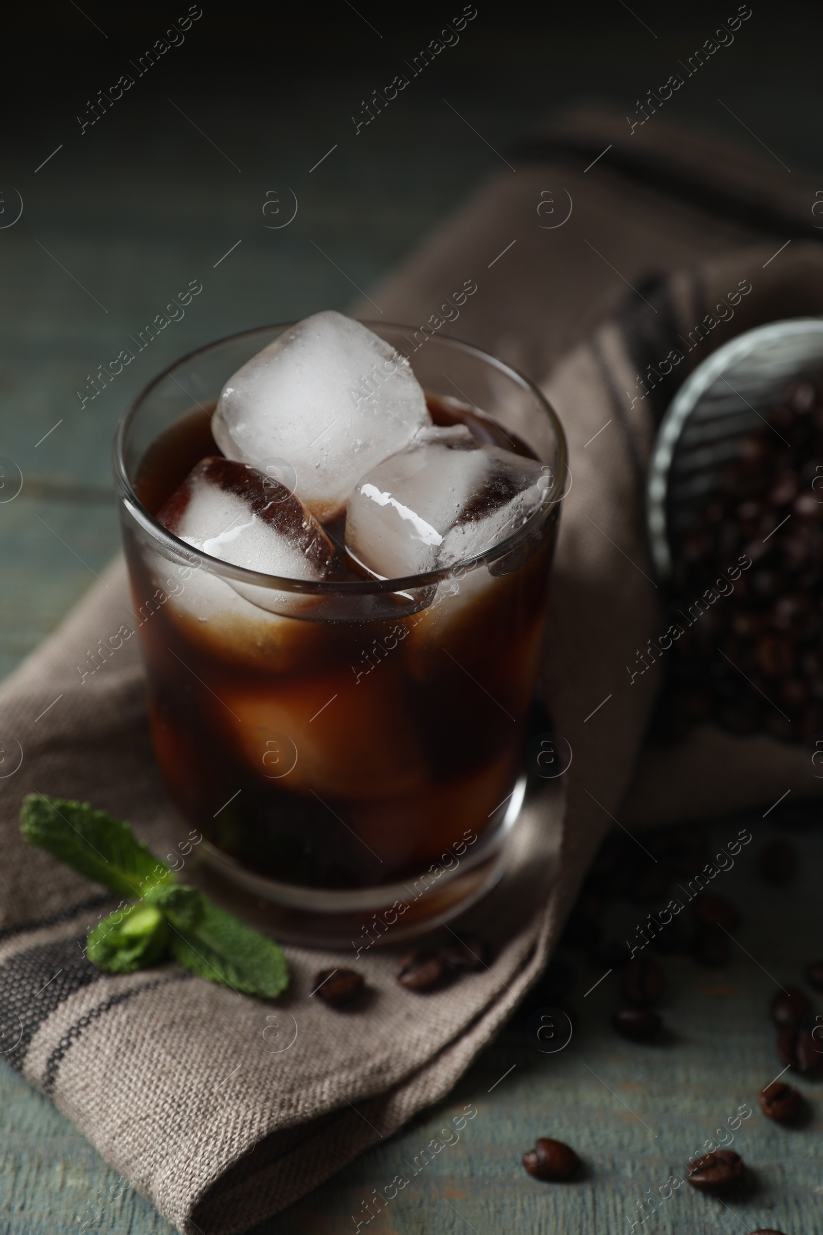 Photo of Glass of delicious iced coffee, beans and mint on light blue table