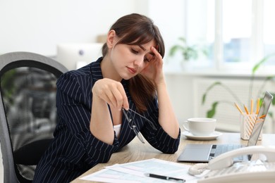 Photo of Overwhelmed office worker sitting at table with laptop and documents indoors