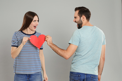 Photo of Couple tearing paper heart on light grey background. Relationship problems