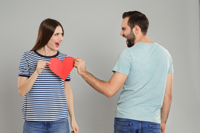 Couple tearing paper heart on light grey background. Relationship problems