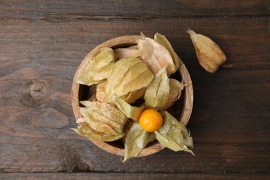 Ripe physalis fruits with calyxes in bowl on wooden table, top view