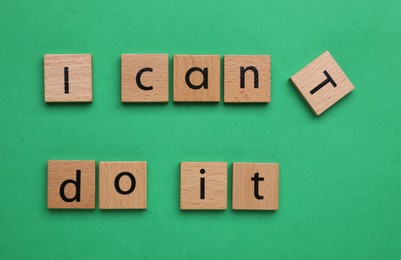 Photo of Motivation concept. Changing phrase from I Can't Do It into I Can Do It by removing wooden square with letter T on green background, top view
