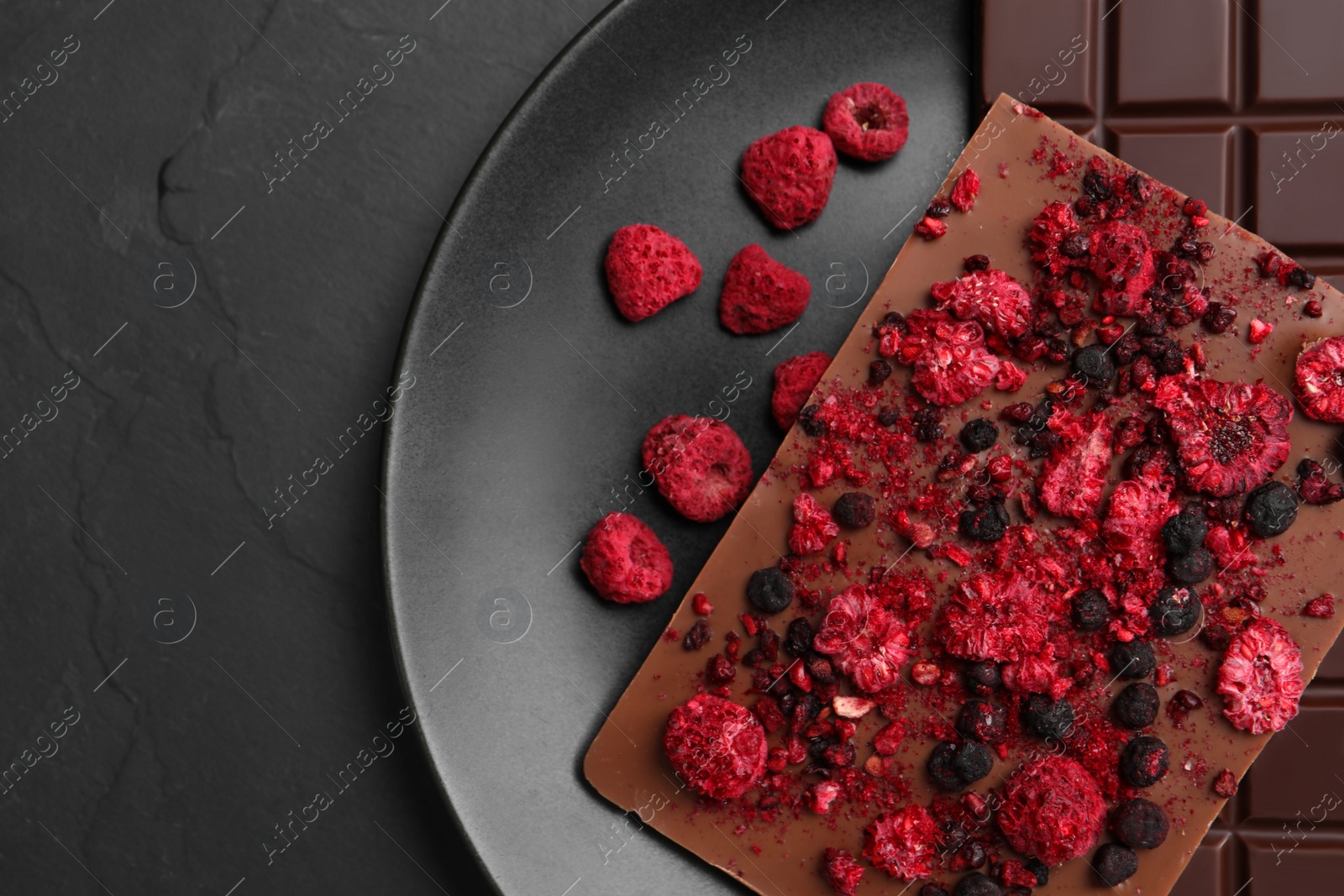 Photo of Plate and different chocolate bars with freeze dried fruits on slate table, top view