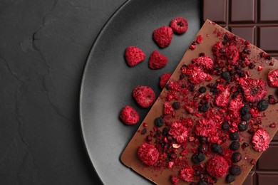 Photo of Plate and different chocolate bars with freeze dried fruits on slate table, top view