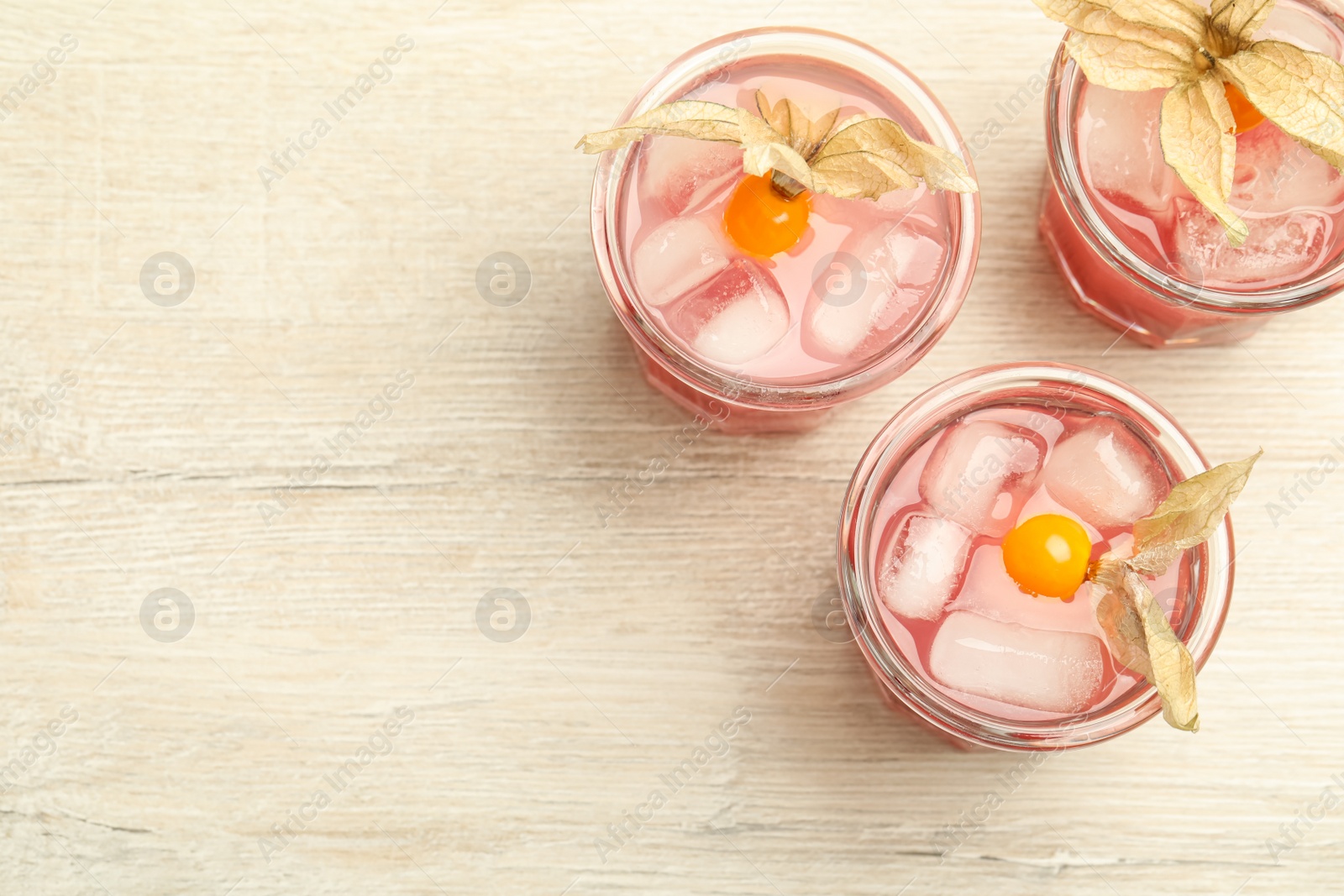 Photo of Refreshing cocktail decorated with physalis fruits on wooden table, flat lay. Space for text