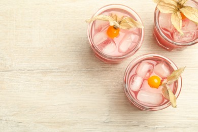 Photo of Refreshing cocktail decorated with physalis fruits on wooden table, flat lay. Space for text