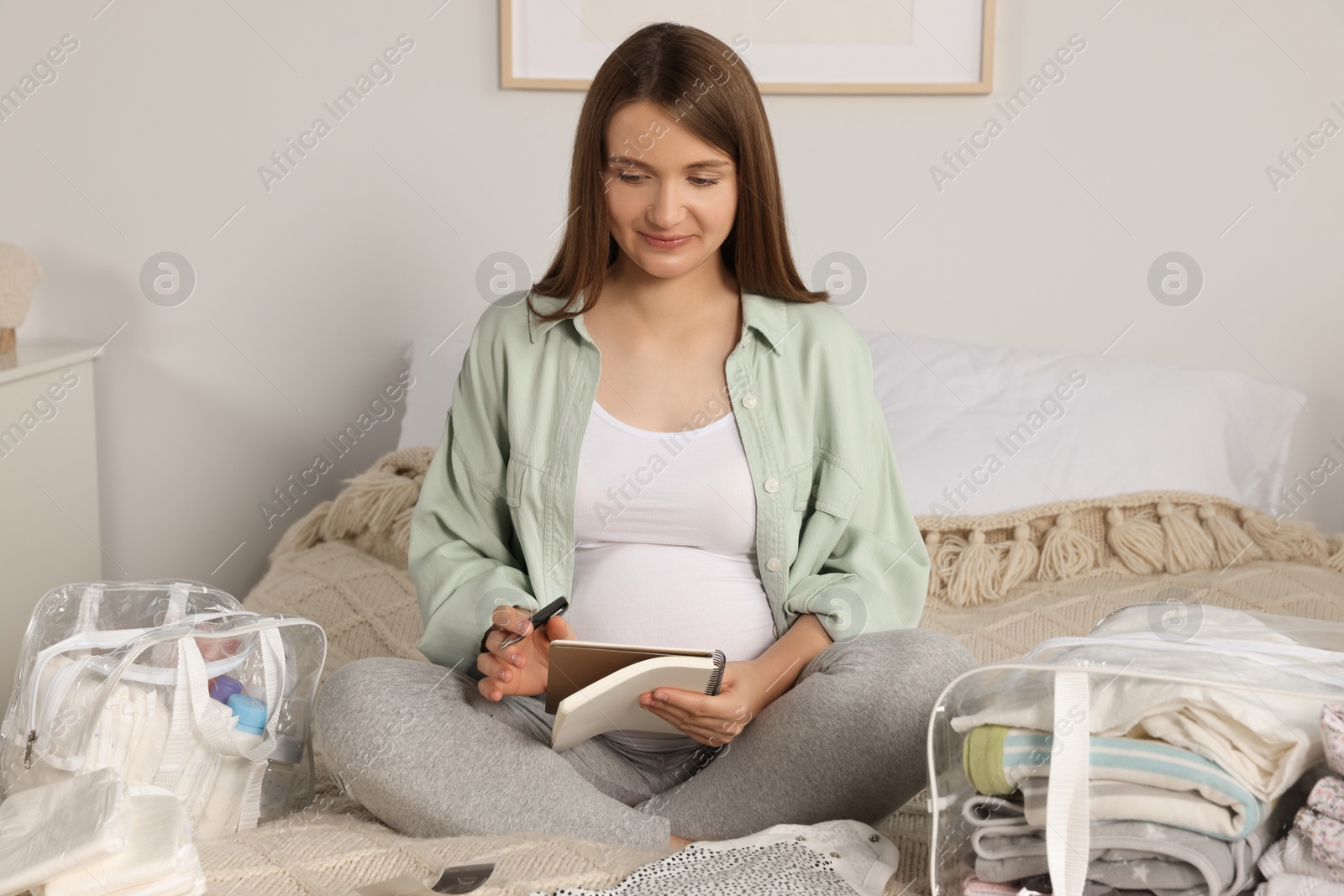 Photo of Pregnant woman preparing list of necessary items to bring into maternity hospital in bedroom