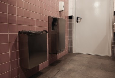 Photo of Hand dryer and trash can on tiled wall in public toilet