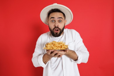 Emotional young man with French fries on red background