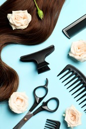 Flat lay composition with professional hairdresser tools, flowers and brown hair strand on light blue background