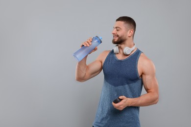 Handsome sportsman with headphones and bottle of water on grey background, space for text