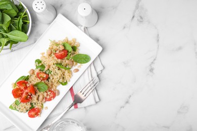Delicious quinoa salad with tomatoes, beans and spinach leaves served on white marble table, flat lay. Space for text