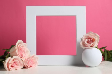 Photo of Stylish presentation for product. Frame, beautiful roses and ball on light table against pink background, space for text