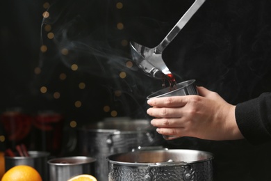 Photo of Woman pouring hot mulled wine into mug against blurred background, closeup