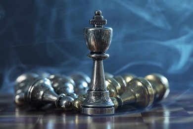 Photo of King among fallen chess pieces on checkerboard against dark background, closeup