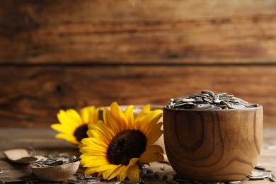 Photo of Bright sunflower and raw seeds on wooden table, closeup. Space for text