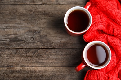 Photo of Flat lay composition cups of hot tea and knitted sweater on wooden background, space for text. Winter drink